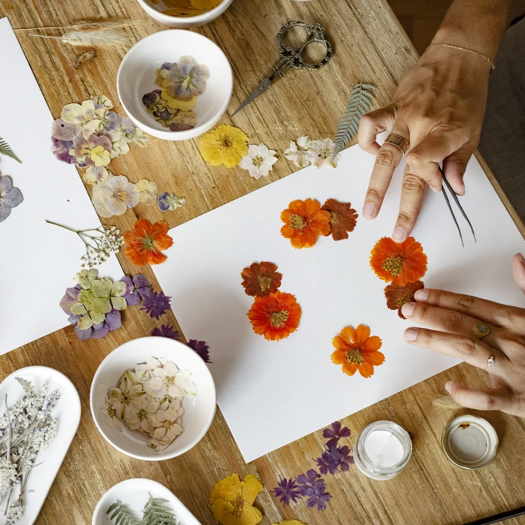 des mains qui arrangent des fleurs pressées sur une feuille blanche